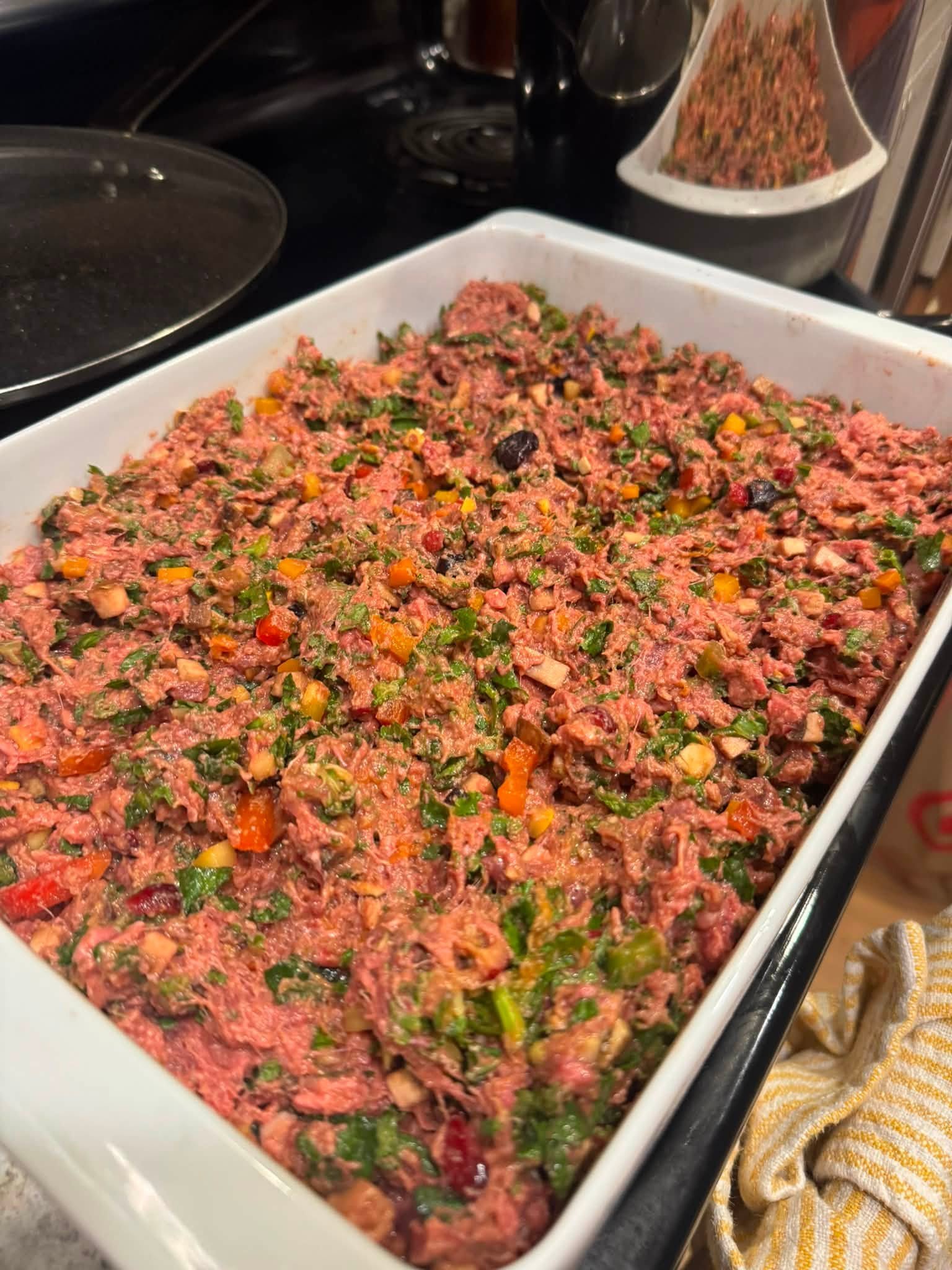 Uncooked beef mixture with chopped vegetables and berries in a casserole dish