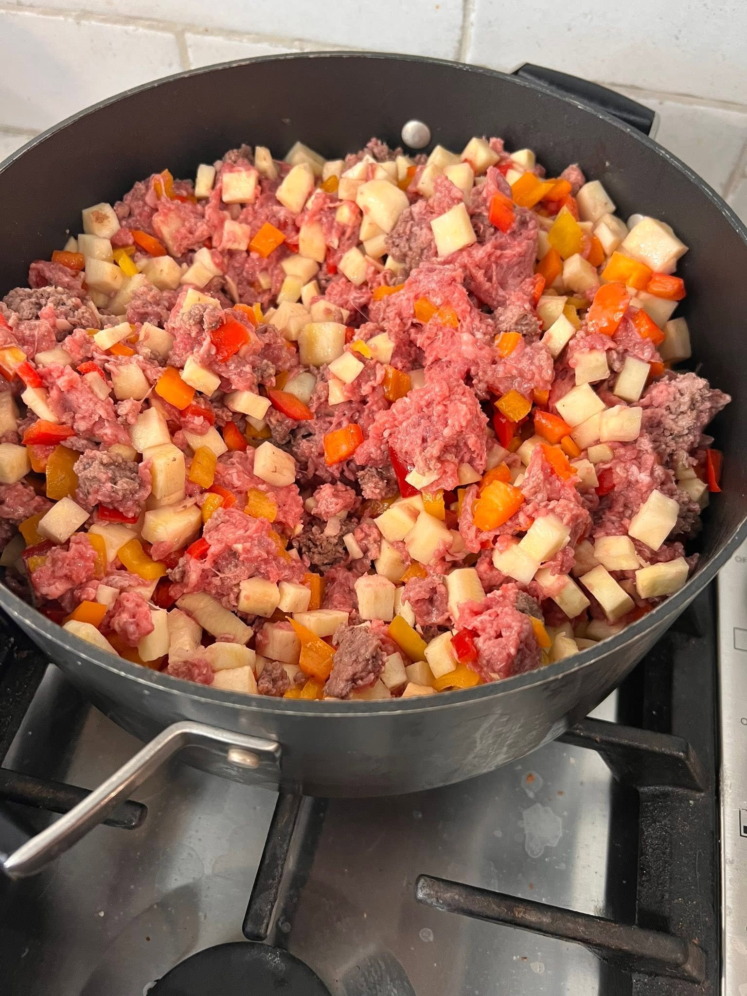 Ground beef, diced sweet potatoes and colorful sweet peppers in a cooking pot