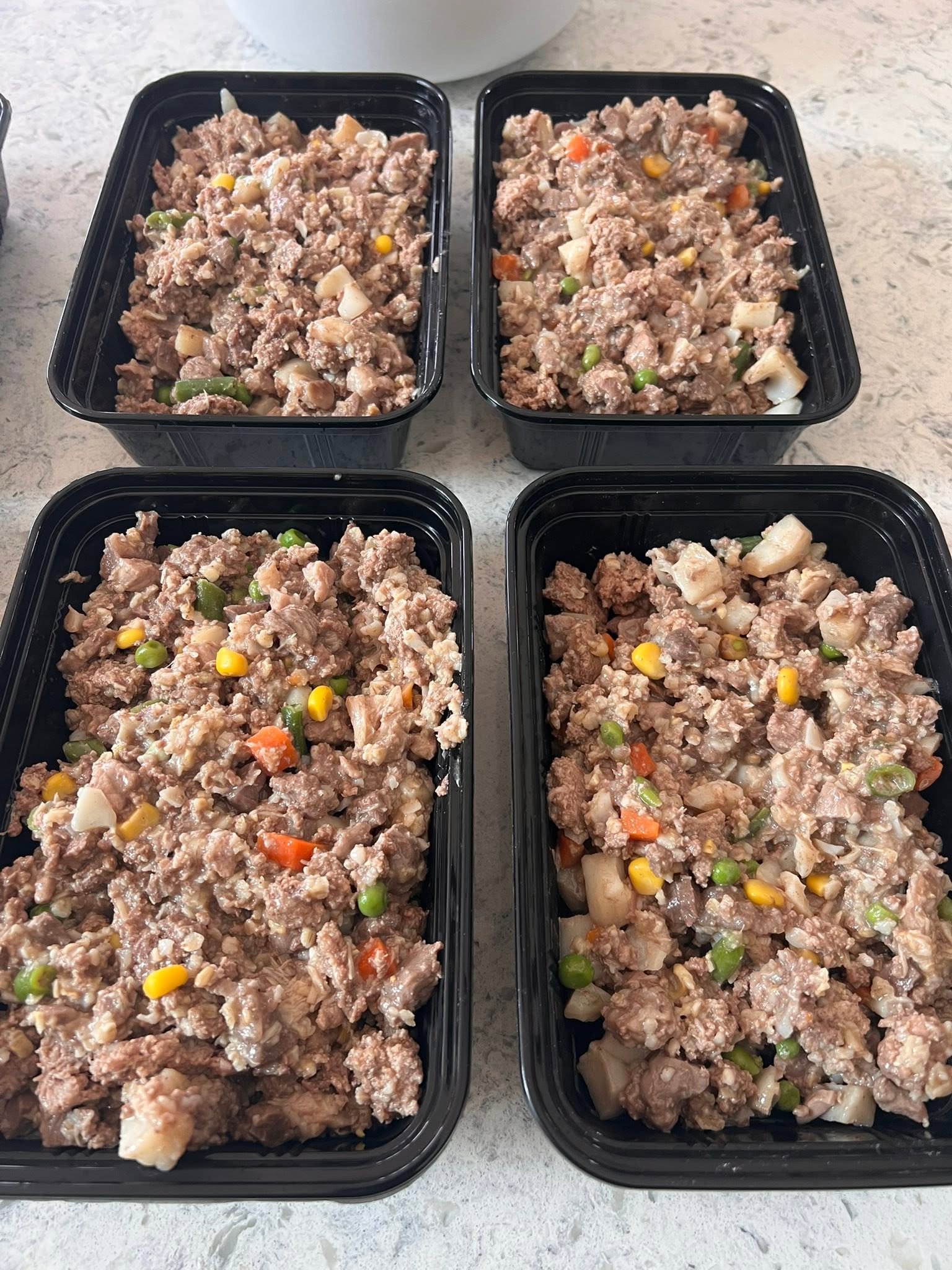 Four black containers filled with a meat and vegetable mixture
