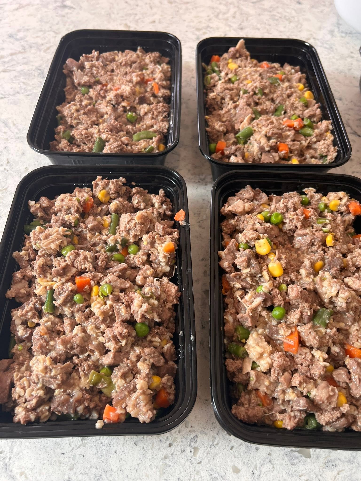 Prepared meat and vegetable portions arranged in black food containers on a counter