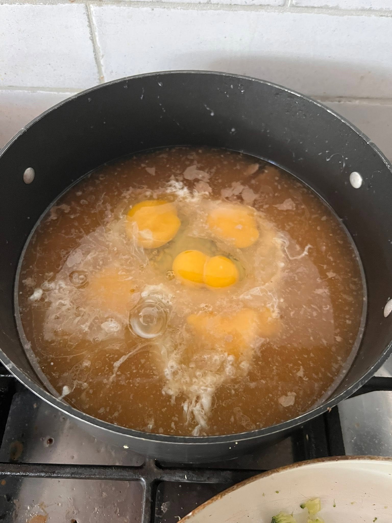 Cracked eggs in liquid in a black cooking pot