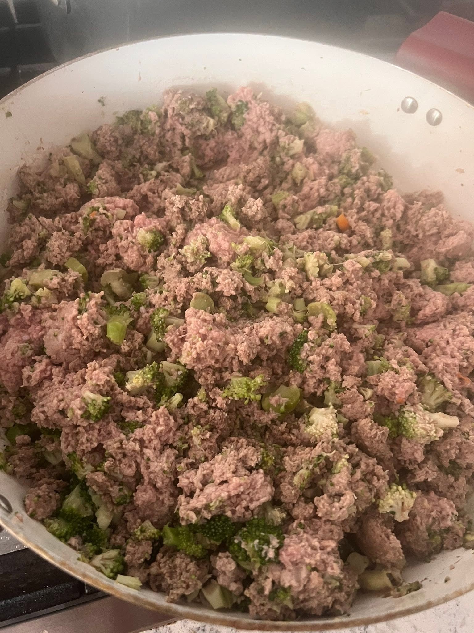 Ground turkey and broccoli during cooking in a white pan
