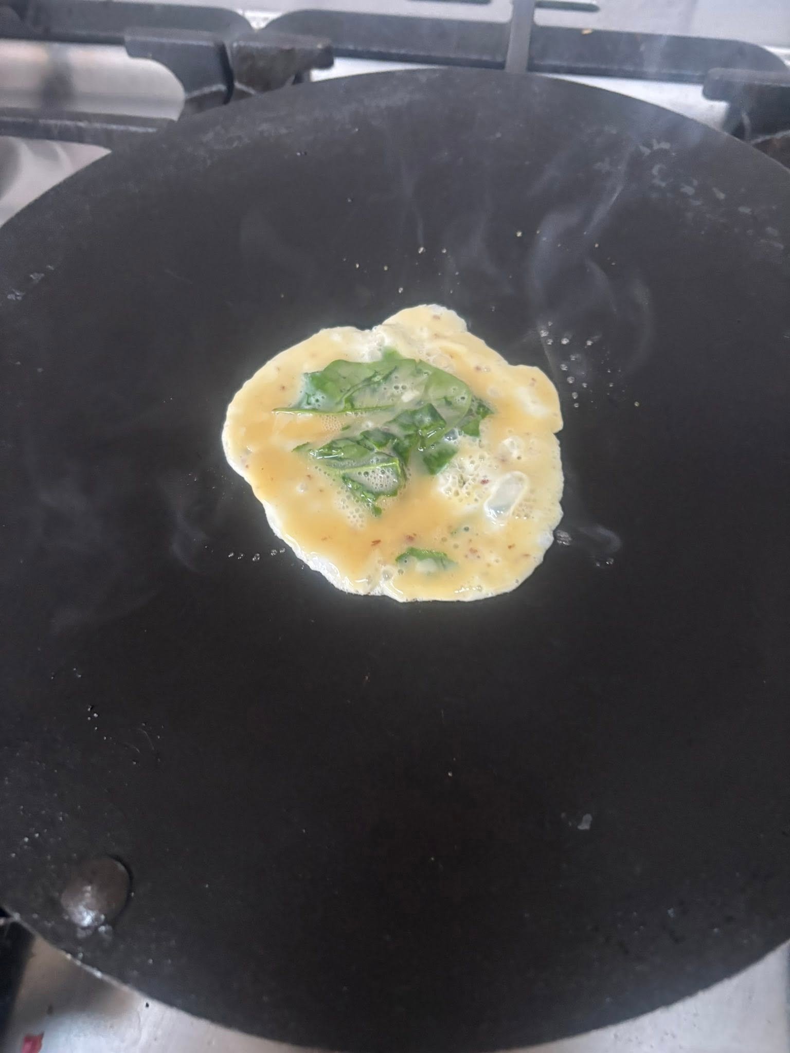 Small egg and spinach omelette cooking in a pan
