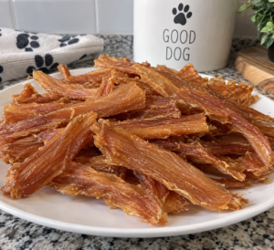 Finished chicken jerky on a plate beside a dog treat jar