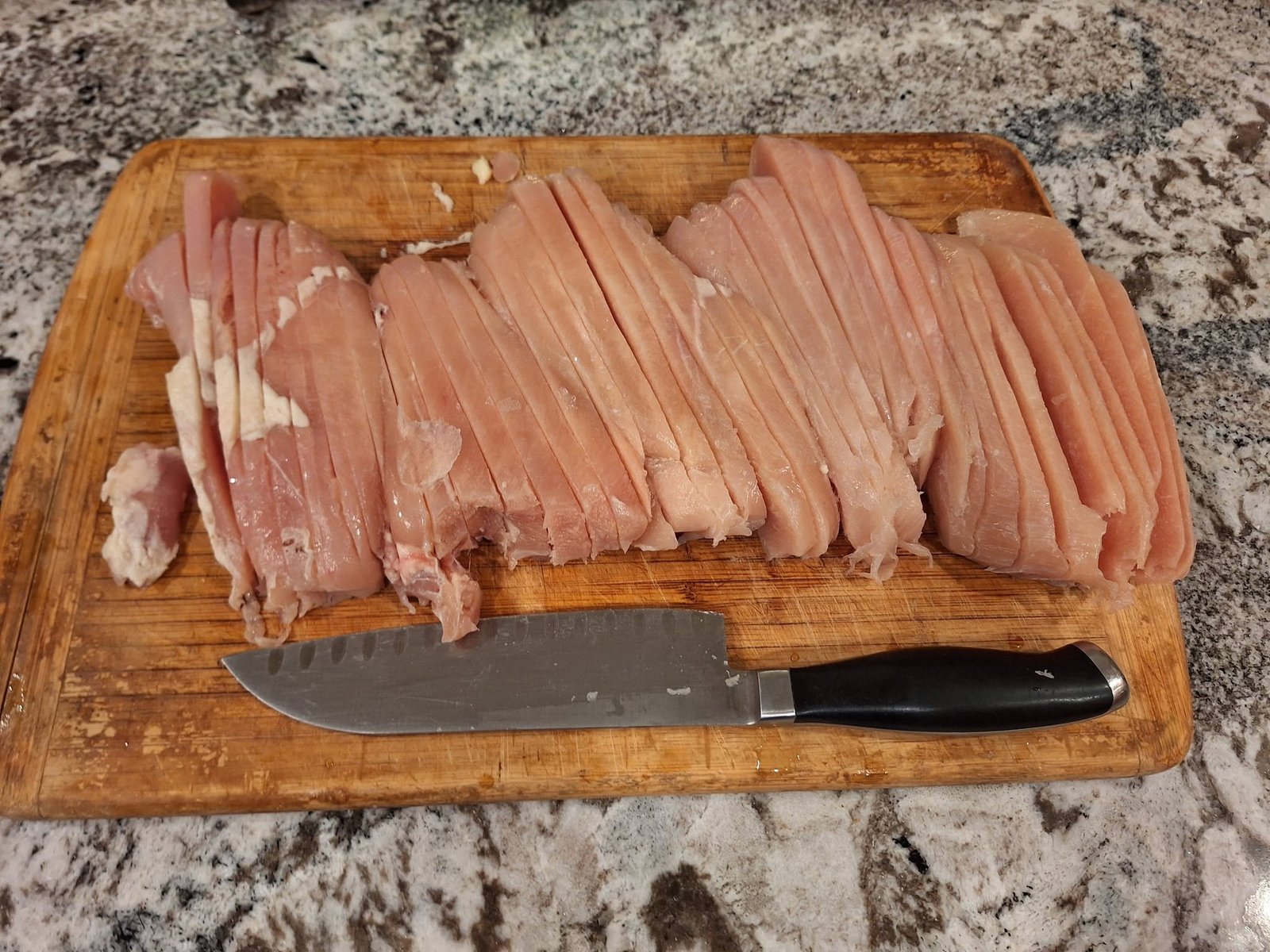 Chicken breast cut into thin strips on a chopping board