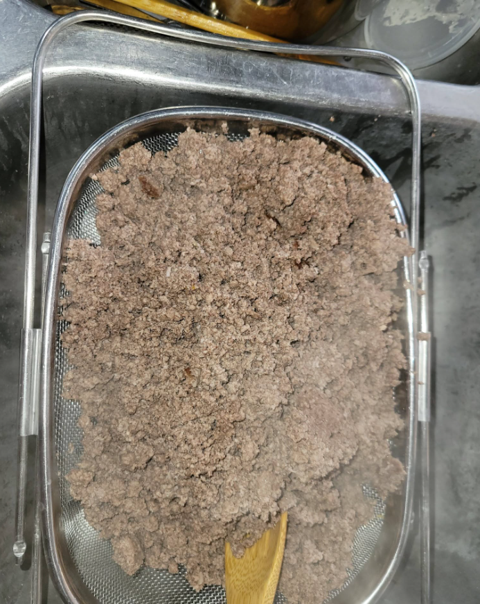 Cooked ground meat in a sieve over a tray