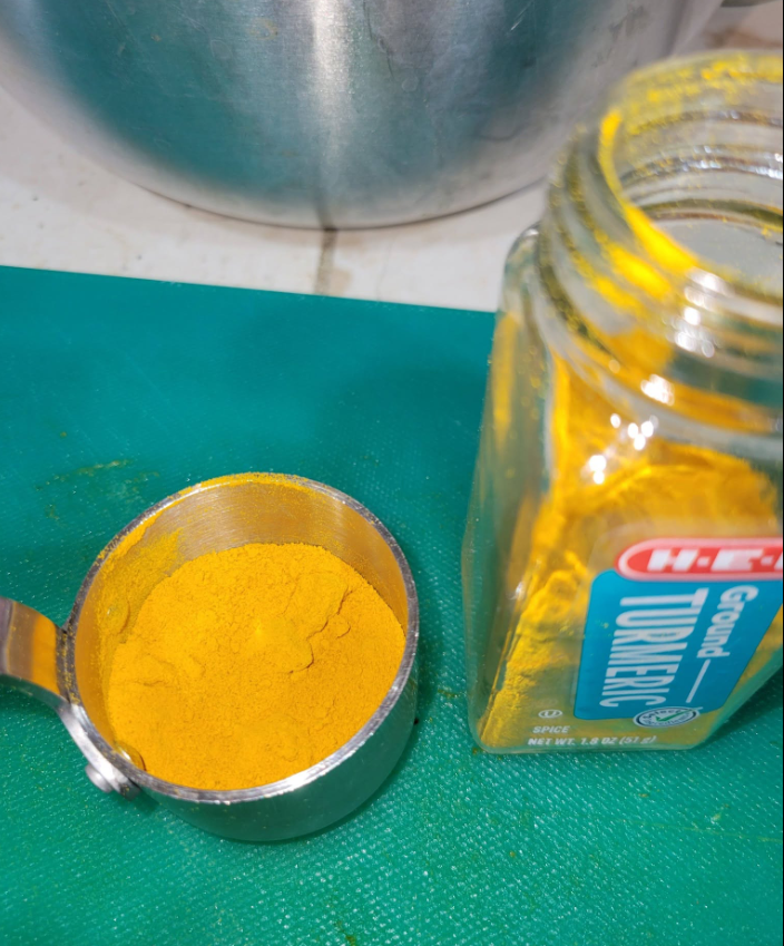 Ground turmeric in a measuring cup beside its jar