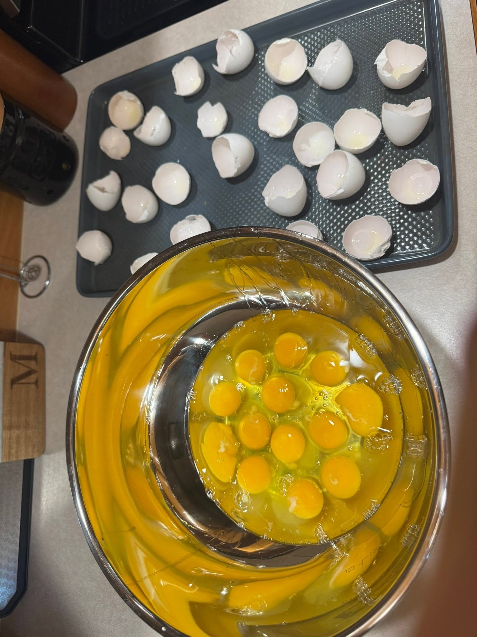 Eggs in a mixing bowl beside eggshells on a tray